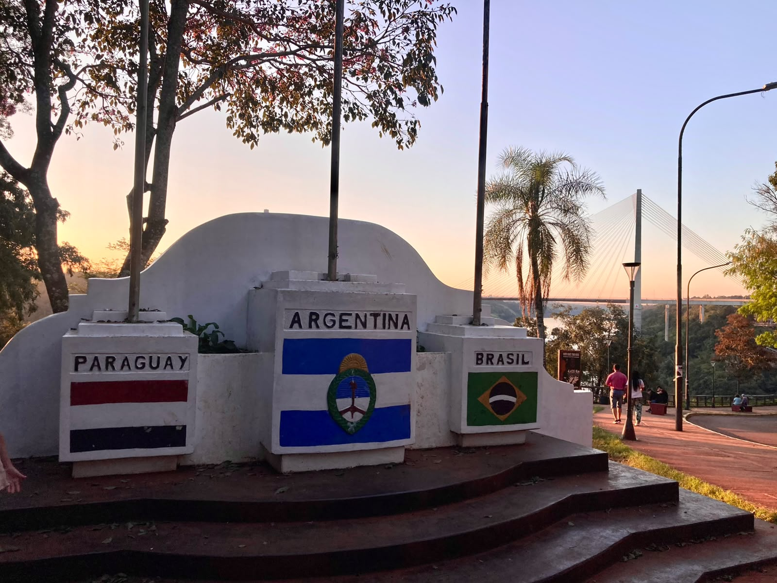 Marco das Três Fronteiras argentino ao entardecer, com bandeiras de Argentina, Brasil e Paraguai